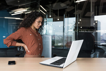 Beautiful Latin American businesswoman working in modern office, worker overtired has severe back...