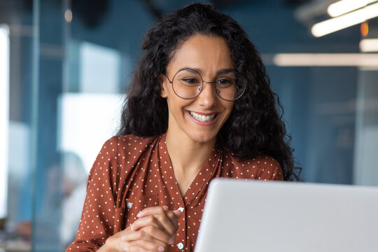 Close-up photo of young beautiful business woman with curly hair and glasses Hispanic woman talking on video call using laptop for remote communication and conference
