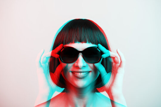 Beauty, fashion concept. Portrait of beautiful and sexy woman with bob style wig holding sunglasses with hand and looking to camera with smile. Red and blue color split effect. Futuristic style