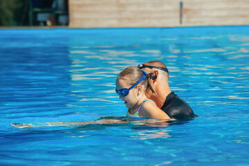 A swimming coach conducts an individual lesson with an 8-year-old girl, teaches her how to swim correctly in the pool water in the warm season