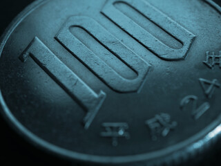 Translation: year of issue 2012. Japanese 100 yen coin close up. Dark blue tinted background. Economy or finance backdrop. Banking in Japan. Scratched textured money from circulation. Macro