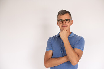 Portrait of confident mature man wearing glasses with hand on chin. Caucasian man wearing blue T-shirt looking at camera and smiling over white background. Success and eyesight concept