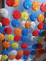 Fototapeta na wymiar Paragüas en el cielo. Decoracion de una calle en la ciudad. Paragüas de colores colgados decoran las calles de una ciudad. Paragüas forman un patron de colores.