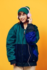vertical photo of a beautiful woman in a jacket and hat in the style of the 90s listening to music with pink headphones holding them with her hands