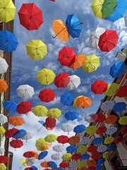 Fototapeta na wymiar Paragüas en el cielo. Decoracion de una calle en la ciudad. Paragüas de colores colgados decoran las calles de una ciudad. Paragüas forman un patron de colores.
