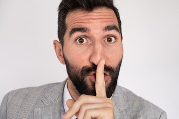 Handsome man with beard calling be silent. Male model in suit touching lips with finger, looking at camera. Portrait, studio shot, gesture concept