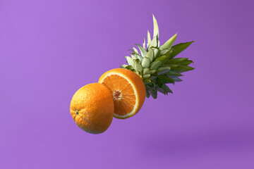 Creative food concept on a purple background. Cut up a falling orange with a pineapple tail.