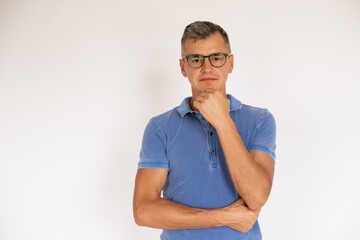 Portrait of thoughtful mature man wearing glasses. Caucasian man wearing blue T-shirt standing against white background. Confidence concept