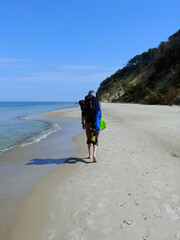 Mężczyzna z plecakiem spacerujący po plaży.