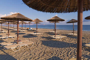 Empty beach with sun loungers and umbrellas in the early morning on a sunny day on the Crete island...
