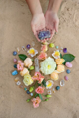 Hands with gemstones and flowers for Crystal Ritual on sand natural background. Esoteric spiritual...