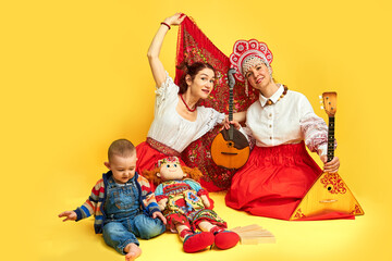 Women musicians in Russian folk dresses with musical instruments on a yellow studio background....