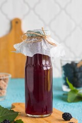 Blackberry syrup for drinks and ice cream in a glass bottle on a wooden board on a turquoise concrete background. Blackberry recipes.