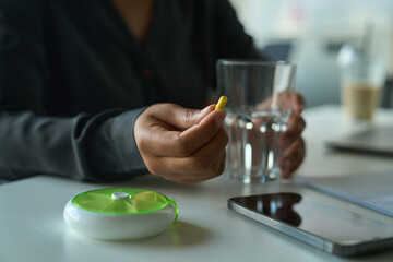 Multiracial female sits at a table and holds a pill and a glass of water