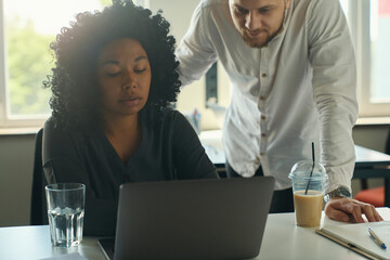 Friendly man in office helping female colleague with work moments