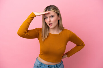 Young caucasian woman isolated on pink background looking far away with hand to look something