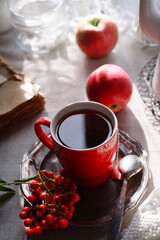 A cup of tea with a bunch of red rowan on metal plate and two apples, autumn morning tea concept.