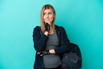 Young sport woman with sport bag isolated on blue background having doubts and thinking