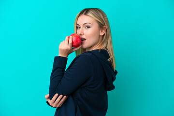 Young caucasian woman isolated on blue background eating an apple