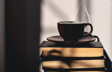 Cup of coffee or tea on top of stack of books with sunlight and shadows