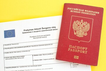 Schengen visa application form in Russian and Lithuanian language and passport on yellow background. Prohibition and suspension of visas for tourists travel to European Union and Baltic States