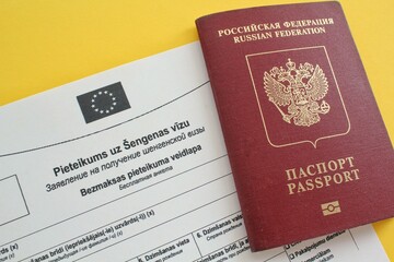 Schengen visa application form in Russian and Latvian language and passport on yellow background. Prohibition and suspension of visas for tourists to travel to European Union and Baltic States concept