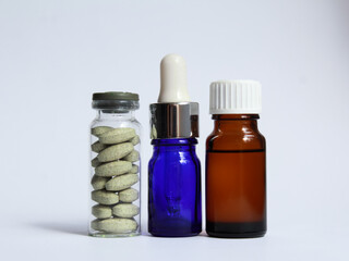 Closed glass jar with green pharmaceutical pills, blue pipette with medical drops and brown pharmaceutical bottle with liquid on white background