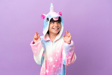 Obraz na płótnie Canvas Little kid wearing a unicorn pajama isolated on purple background with fingers crossing