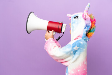 Little kid wearing a unicorn pajama isolated on purple background shouting through a megaphone
