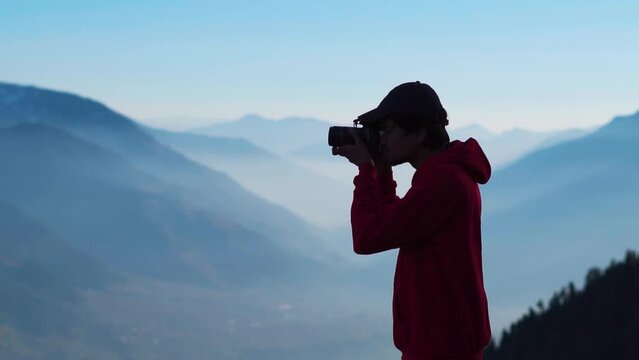 Silhouette shot of an Indian photographer looking at the screen of the camera after taking picture in front of the foggy mountains at Manali in Himachal Pradesh, India. Photographer reviews his photos