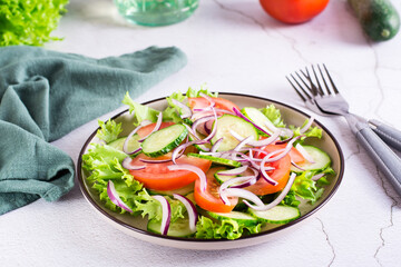 Tomato, cucumber, onion, lettuce salad on a plate on the table. Vegetarian food
