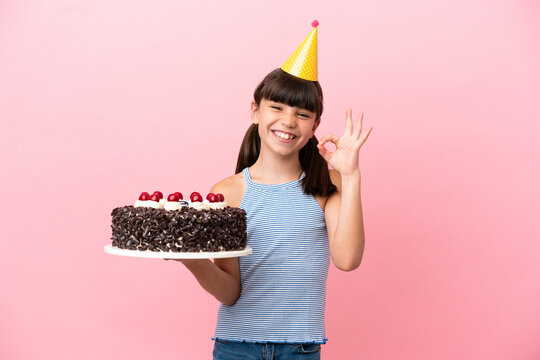 Little caucasian kid holding birthday cake isolated in pink background showing ok sign with fingers
