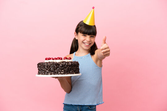 Little caucasian kid holding birthday cake isolated in pink background with thumbs up because something good has happened