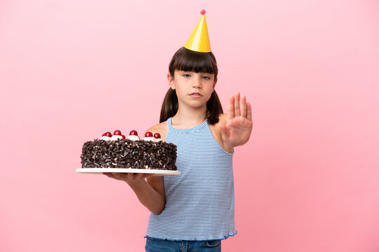 Little caucasian kid holding birthday cake isolated in pink background making stop gesture