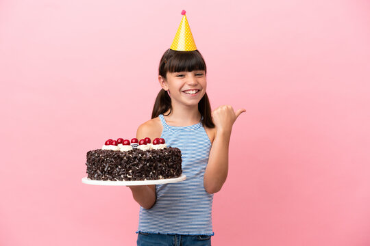 Little caucasian kid holding birthday cake isolated in pink background pointing to the side to present a product