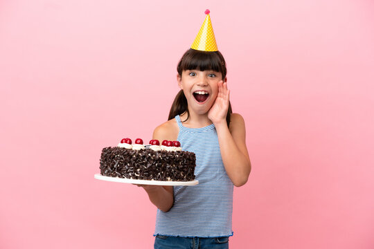 Little caucasian kid holding birthday cake isolated in pink background with surprise and shocked facial expression
