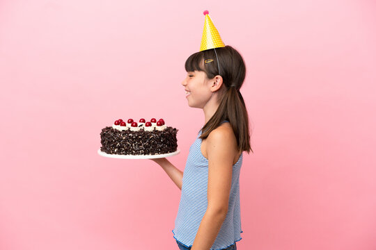 Little caucasian kid holding birthday cake isolated in pink background laughing in lateral position