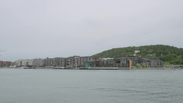 A walk along the river. Action.Green mountains next to which houses stand on the shore and you can see the gray sky overhead with clouds.