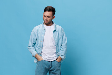 Pensive upset thoughtful tanned handsome man in casual basic t-shirt hold hands on jeans pocket posing isolated on blue studio background. Copy space Banner Mockup. People emotions Lifestyle concept