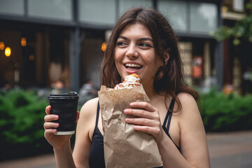 A young woman with a croissant and a cup of coffee on a city walk.