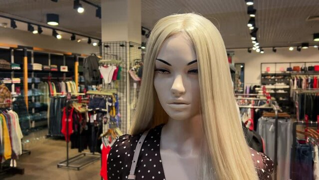 Beautiful female mannequin with blonde hair in dress stands in the window of a women's clothing store