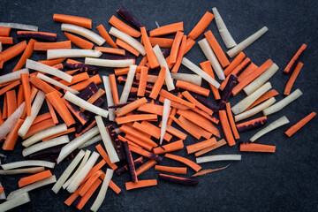 Scattered slices of chopped fresh colored carrots on a dark background. Food background.