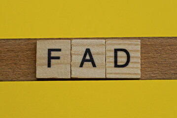  the gray word fad of gray small wooden letters lies on a yellow table