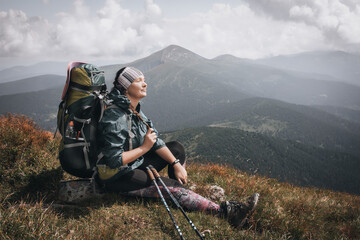 Girl hiker with a backpack stands on a rock in the mountains. Trekking life. Hike through the...
