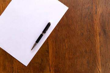 Pen on blank sheet. Wooden table. Top view.