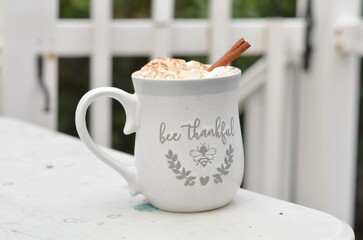 cup of coffee with cinnamon sticks outside with white picket fence