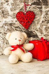 White Teddy bear with red heart and gift box on grey wall background