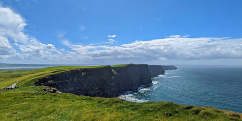 Panoramic view of the Cliffs of Moher sightseeing spot in Ireland under a cloudy blue sky and irish...