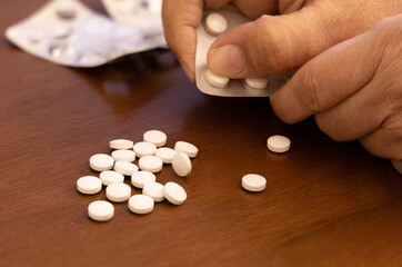 Fototapeta na wymiar Hand picking medicine pills on wooden surface. Selective focus.
