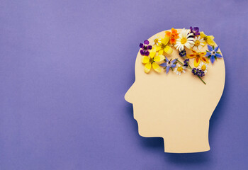 World mental health day concept. Human head symbol and flowers on a violet background. Copy space